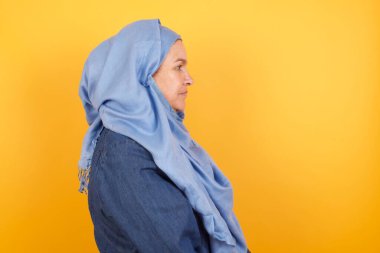 Orta yaşlı, sağlıklı, saf tenli, tesettürlü Müslüman bir kadının profili derin düşüncelere dalmış.