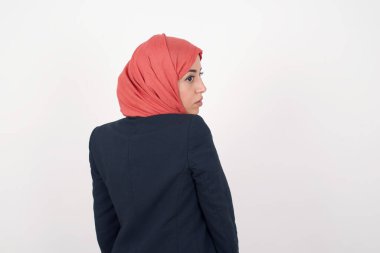 Güzel Müslüman bir kadının arka tarafı siyah ceket ve tesettür giyer ve gri duvara dayanır. Stüdyo Çekimi. 