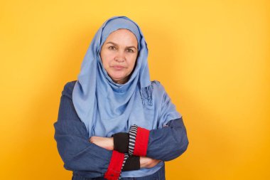Güzel orta yaşlı müslüman kadın portresi pozitiftir, kollarını kavuşturur, mutlu ve kendinden emin hisseder, arka planda izole olur.