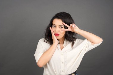 Güzel esmer kadın, gelişigüzel giyinmiş. Gri arkaplanda duruyor. 