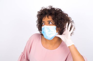 Yüz maskesi takan ve beyaz stüdyo arka planında izole edilmiş, günlük giysiler giyen bir kadın.