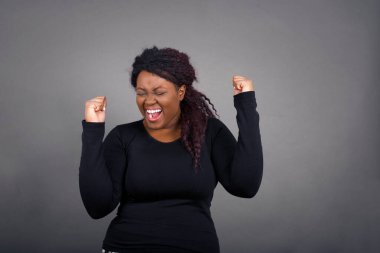 Kafkasyalı esmer Afrikalı Amerikalı kadın, günlük kıyafetleriyle başarısını ve zaferini sevinçle kutluyor. Hedeflerine ve hedeflerine ulaşmaktan mutlu olan şanslı kadın. Olumlu duygular, duygular.