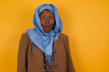 Çekici genç Afrikalı Amerikalı Müslüman kadın ağzı açık ve ağzı açık bir şekilde şaşkınlık içinde, arkadaşının hikayesini dinlerken 