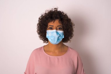 Yüz maskesi takan ve beyaz stüdyo arka planında yalnız poz veren kadın.