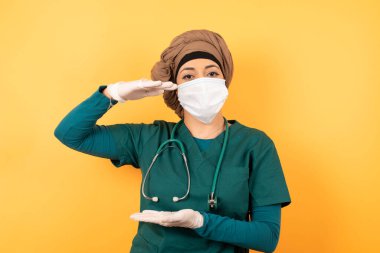 Yeşil üniformalı, genç, Müslüman doktor kadın izole edilmiş arka plan jestleri ile büyük ve büyük bir işaret, ölçü sembolü gösteriyor. Kameraya bakıp gülümsüyor. Ölçüm konsepti.