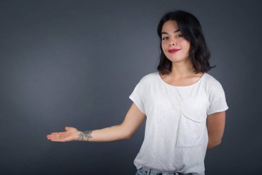 Güzel genç bir kadının portresi. Gri arka planda hoş bir jest yaparak kollarını açmış..