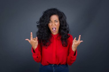 Kıvırcık saçlı, kırmızı tişörtlü neşeli esmer kadın yüksek sesle bağırıyor ve kollarını kaldırarak ya da rock hareketleriyle gösteriyor. Konserde olmanın heyecanını ifade ediyor..