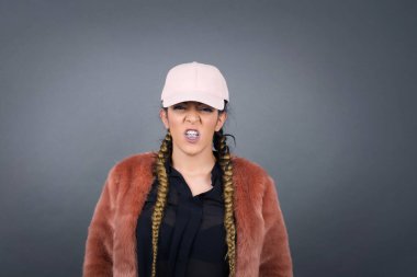 Çılgın deli kadın dişlerini öfkeyle sıkar, gelen sesten rahatsız olur, şık kıyafetler giyer, gri arka planda izole olur. Olumsuz duygu kavramı.