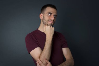 Yüz ifadeleri ve duygular. Düşünceli genç adam, gündelik giysiler içinde kafasının altında el ele tutuşuyor. Arkadaşının doğum günü partisinde ne giyeceğine karar veremezken şüpheli bakışlar atıyor. 