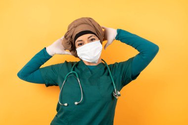 Güven ve cinsel ilişki konsepti. Yüz maskesi takan, tıbbi üniforma giyen, kendinden emin bir ifadeyle gülümseyen ve ellerini başının üzerinde tutan kadın portresi..