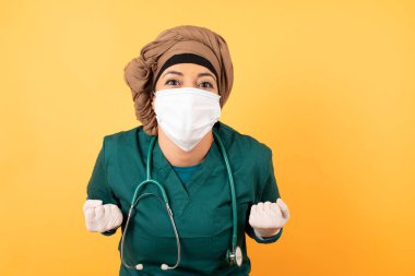 Doktor üniformalı bir kadının yakın plan portresi. Parlak arka planda izole edilmiş yumruklarını kaldırıyor. Büyük gözler. 