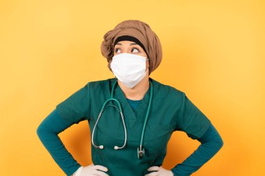 Yüzüne maske takmış neşeli Arap kadın bir şeyler düşünürken belini kaldır. Ellerini kalçaya koy, yüz ifadenden şüphe et. Gri duvara yaslanmış bir şey olup olmadığını merak ediyorum..