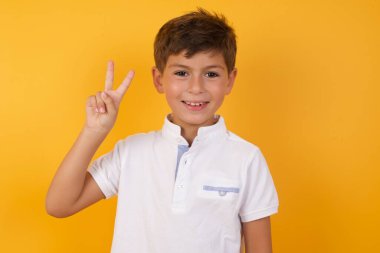 Sarı duvara karşı zafer gösteren sevimli çocuk.  