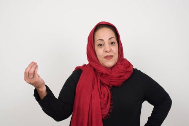 What the hell are you talking about. Shot of frustrated woman gesturing with raised hand doing Italian gesture, frowning, being displeased and confused with dumb question. Middle-aged Arab woman wearing head scarf posing in studio