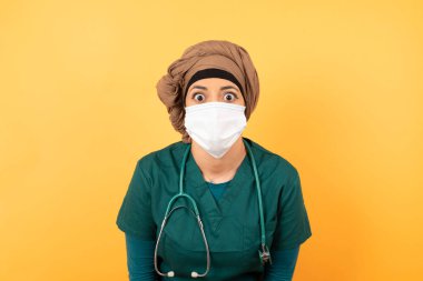 Ağzı açık duygusal doktor kadın şaşkınlık ve korku ifade ediyor, beyaz beton arka planda poz veriyor, kameraya bakıyor. Beklenmedik haberler ve insani tepkiler.