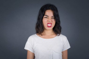 Çılgın deli kadın dişlerini öfkeyle sıkar, gelen sesten rahatsız olur, şık kıyafetler giyer, gri arka planda izole olur. Olumsuz duygu kavramı.