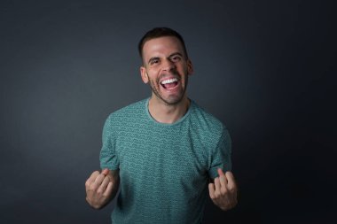 Yakışıklı beyaz adamın kapalı portresi yumruklarını kaldırıyor parlak gri arka planda büyük gözler ve geniş bir ağız.