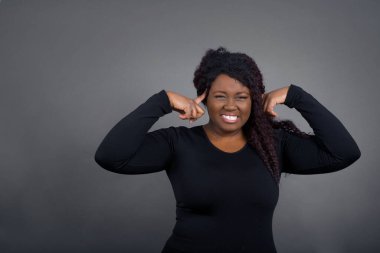 Genç, güzel, Afro-Amerikalı bir kadın gündelik giysiler içinde ciddi bir bakışla bir fikre odaklanmış, her iki işaret parmağı da kapalı alnını işaret ederek düşünüyor..