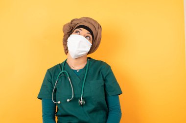 Büyüleyici genç Müslüman kadın portresi yeşil üniformalı gizemli bir gülümsemeyle yukarı bakıyor..