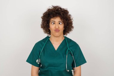 Komik komik, güzel Arap doktor kadın tıbbi üniforma giyiyor, şaşı bakıyor, garip bir ifadeyle eğleniyor, suratını ekşitiyor.
