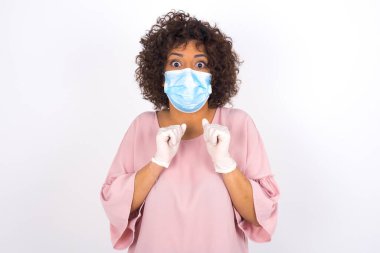 Yüz maskesi takan ve günlük kıyafet giyen kadın beyaz stüdyo arka planında izole edilmiş.