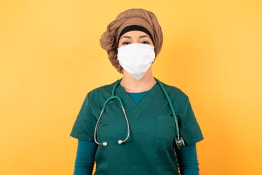 Yeşil tıp üniformalı, kendinden emin bir ifadeyle gülümseyen güzel Müslüman kadın portresi. 