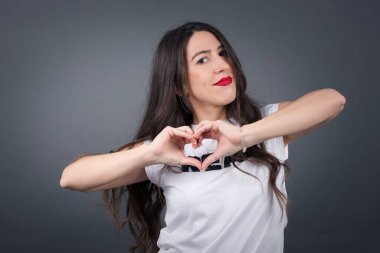 Gri arka planda kalbini gösteren güzel bir kadın.  