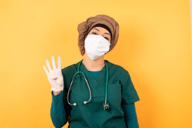 Yeşil üniformalı, genç, güzel, Müslüman doktor dört numaralı parmaklarıyla duvara yaslanmış gülümseyen, kendinden emin ve mutlu bir kadın..