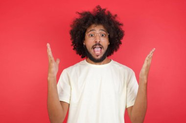 Afro saçlı genç adamın kırmızı duvara karşı kafası karışık.   