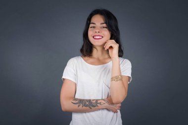 Yüzüne yakın eli gri duvarda duran neşeli, güzel, beyaz bir bayan resmi. İyi haberleri dinledikten sonra kameraya mutlu bir ifadeyle bakmak. Kendine güvenen kız..