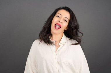 Güzel esmer kadın, gri arka planda gelişigüzel giyinmiş dil gösteriyor..  