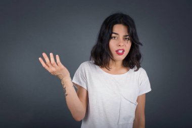 What the hell are you talking about, nonsense. Studio shot of frustrated  woman gesturing with raised palm, frowning, being displeased and confused with dumb question over gray wall.