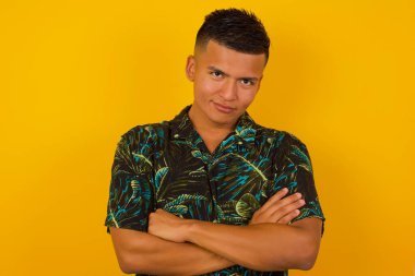 Genç, yakışıklı İspanyol erkek portresi pozitiftir, kollarını kavuşturur, mutlu ve kendinden emin hisseder, rahat kıyafetler giyer, arka planda soyutlanır..