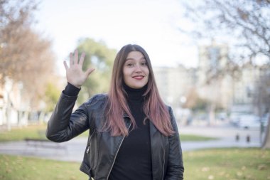 Genç ve güzel bir kadın parkta elini gösteriyor.