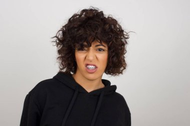 Çılgın deli kadın dişlerini öfkeyle sıkar, gelen sesten rahatsız olur, şık kıyafetler giyer, gri arka planda izole olur. Olumsuz duygu kavramı.