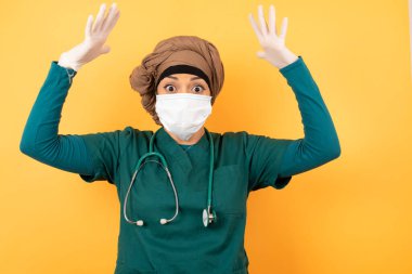 Yeşil üniformalı güzel Müslüman kadın portresi kameraya heyecanla bakıyor, ellerini başının üstüne kaldırıyor, beklenmedik bir şey fark ediyor, duvarın üzerinde izole edilmiş..