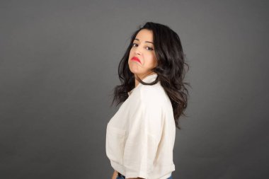 Güzel küstah esmer kadın gündelik giyinmiş. Gri arkaplanda duruyor. 