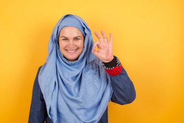 Orta yaşlı tesettürlü çekici müslüman kadın işaret diliyle onaylıyor, neşeli bir ifadesi var, iyimser.. 