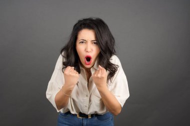 Güzel esmer kadın bağırıyor. Gri arkaplanda duruyor. 