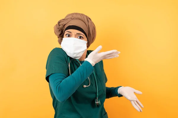 Beautiful European doctor girl pointing aside with both hands showing something strange and saying: I don\'t know what is this. Standing against gray background. Advertisement concept.