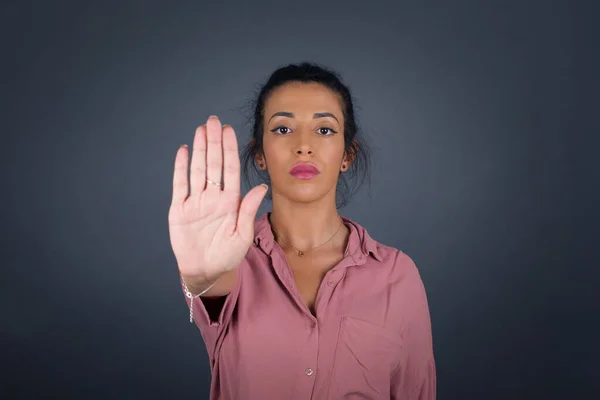 Young beautiful brunette woman doing stop gesture with palm of the hand. Warning expression with negative and serious gesture on the face isolated over gray background.