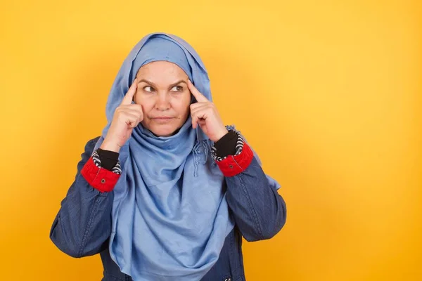 思慮深い表情のヒジャブの夢のような中年のイスラム教徒の女性は 顔の近くに手を保ち 何か楽しいものについて考え 壁にポーズ — ストック写真