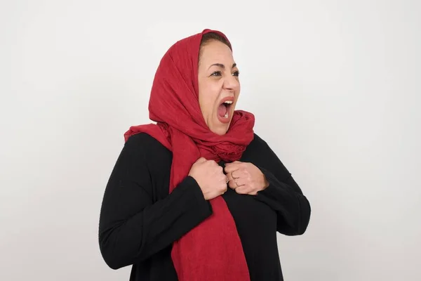 成熟的穆斯林妇女头戴头巾 头戴头巾 站在灰墙边 兴奋而高兴地取得了胜利 紧紧抓住拳头 兴奋地尖叫着 高兴地在大学通过了所有的考试 成功的人 — 图库照片