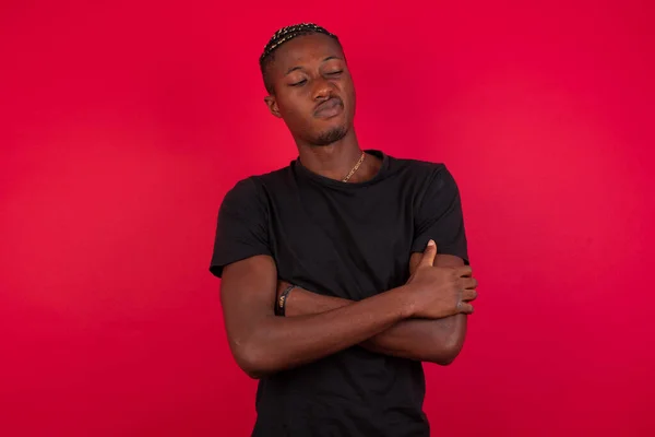 Picture of angry young African American man wearing black t-shirt over red background man crossing arms. Looking at camera with disappointed expression.