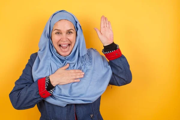 後悔しないことを誓います ハッピーな 中年のイスラム教徒女性の肖像画 ヒジャブで片腕を上げ 誓いを立て 真実を語り 背景の上に立ってあなたが信じたいと望むようにハッピーに手を握る — ストック写真