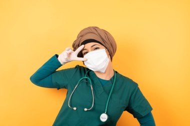  Flört konseptini kutluyoruz. Yeşil üniformalı güzel Müslüman kadın, duvarın karşısında duran V işaretini gösteriyor..