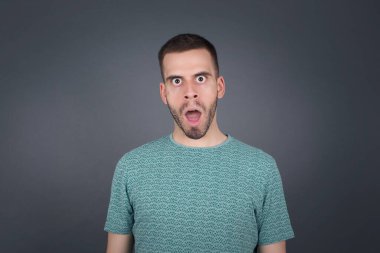 Ağzı açık duygusal çekici bir adam büyük bir şaşkınlık ve korku ifade ediyor, beyaz beton arka plana karşı duruyor, kameraya bakıyor. Beklenmedik haberler ve insani tepkiler.
