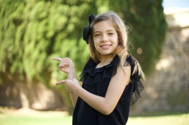 Siyah elbiseli çekici genç kız, neşeli ve şaşkın bir ifadeyle, ağzı açık, parkta inanılmaz bir şey gösteriyor. 