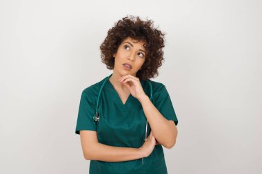 Yüz ifadeleri ve duygular. Düşünceli, Arap doktor kadın. Tıp üniforması giyen, kafasının altında el ele tutuşan, kuşkulu bakışları olan, arkadaşının doğum günü partisinde ne giyeceğine karar veremeyen..