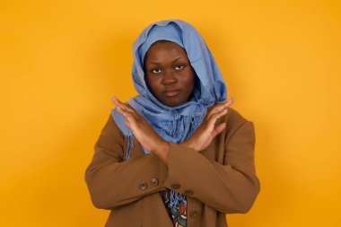 Genç, güzel, Afro-Amerikan Müslüman bir kadın. Günlük giysiler giyip izole edilmiş arka planda duruyor. Reddedilme ifadesi olumsuz işaret göndererek el ele tutuşuyor mu?.